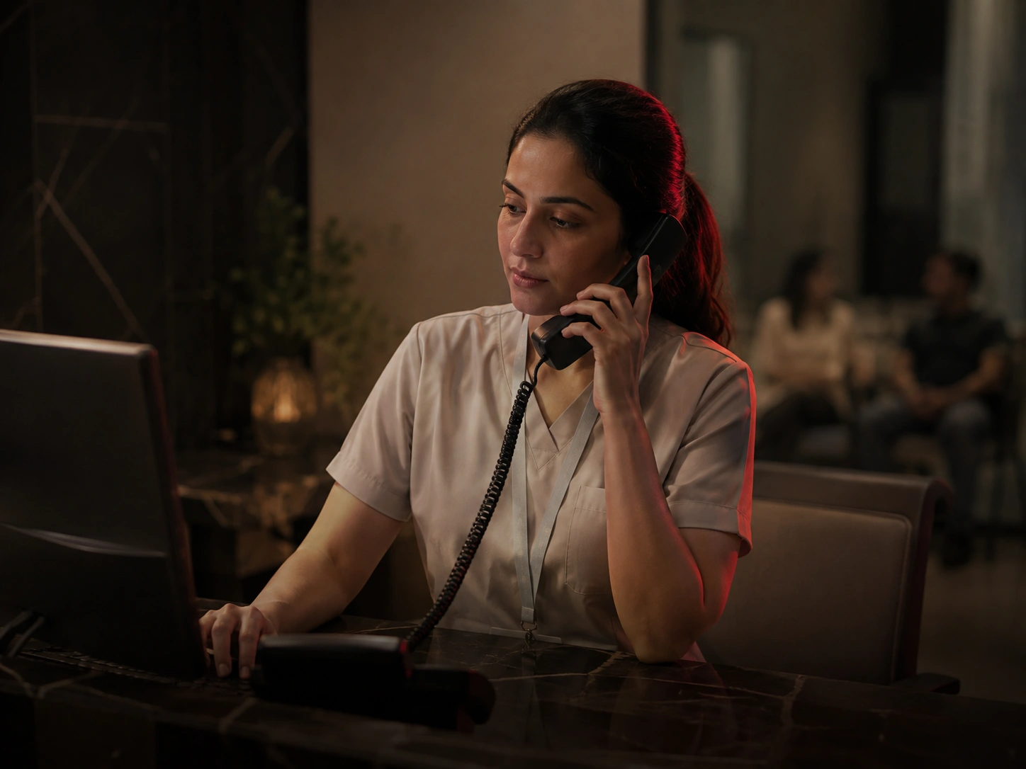 Clinic receptionist on the phone at a desk while patients wait