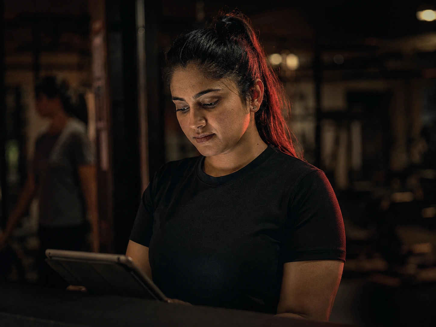 Gym owner checking enquiries on a tablet on the training floor at night